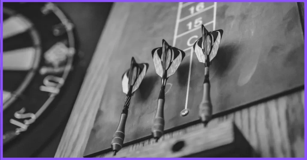  A photo of a dart board with colorful darts and a score sheet on a wooden table. (Best Dart Boards for Garage)