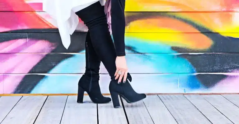 A person wearing high-heeled boots walking on a wooden floor in front of a colorful mural.