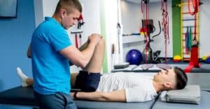 A therapist helping a patient with a leg exercise in a gym setting.