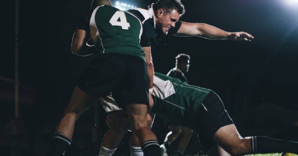 a soccer game in progress, with two players in green and white jerseys jumping up to head the ball, and a goal and a dark sky in the background.