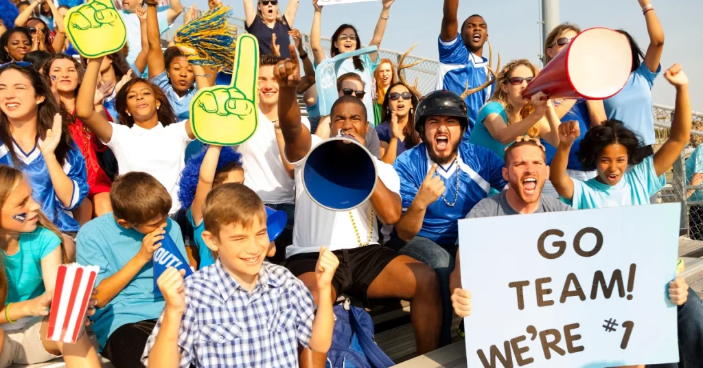 A group of enthusiastic sports fans holding foam fingers, megaphones, and signs at a sports event. (Are Sports Rigged)