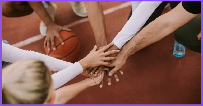 A photo realistic image of a group of people’s hands in a huddle on a basketball court.