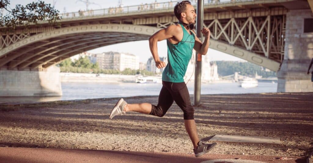 A man in green sportswear running on a dirt path under a green bridge. (Running Clothes by Temperature)