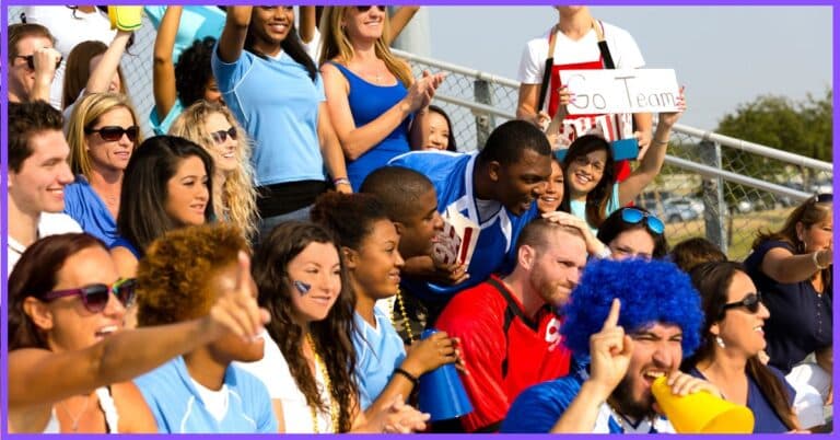 A group of people at a sports event in the stands, cheering and holding a sign that says “Go Team!