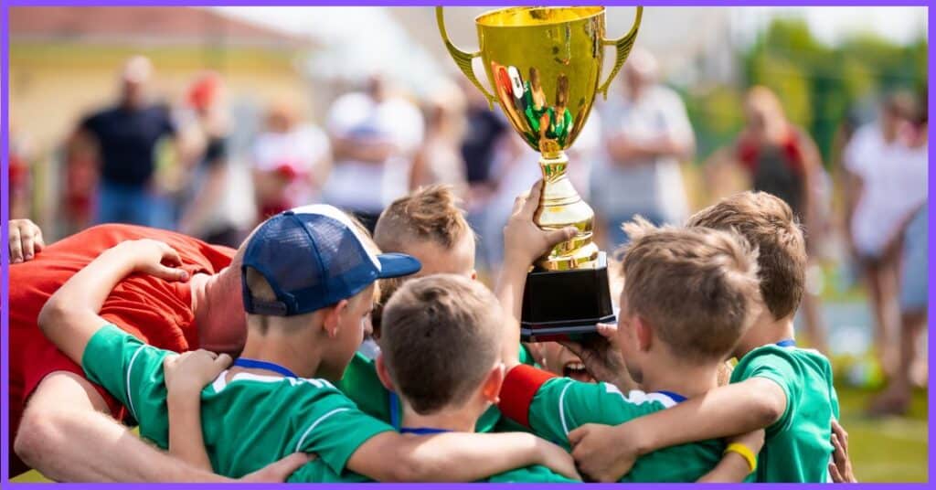 A group of young boys in green jerseys holding a large gold trophy on a grassy field, celebrating a victory over a red team.  (What State Has the Most Pro Sports Teams)