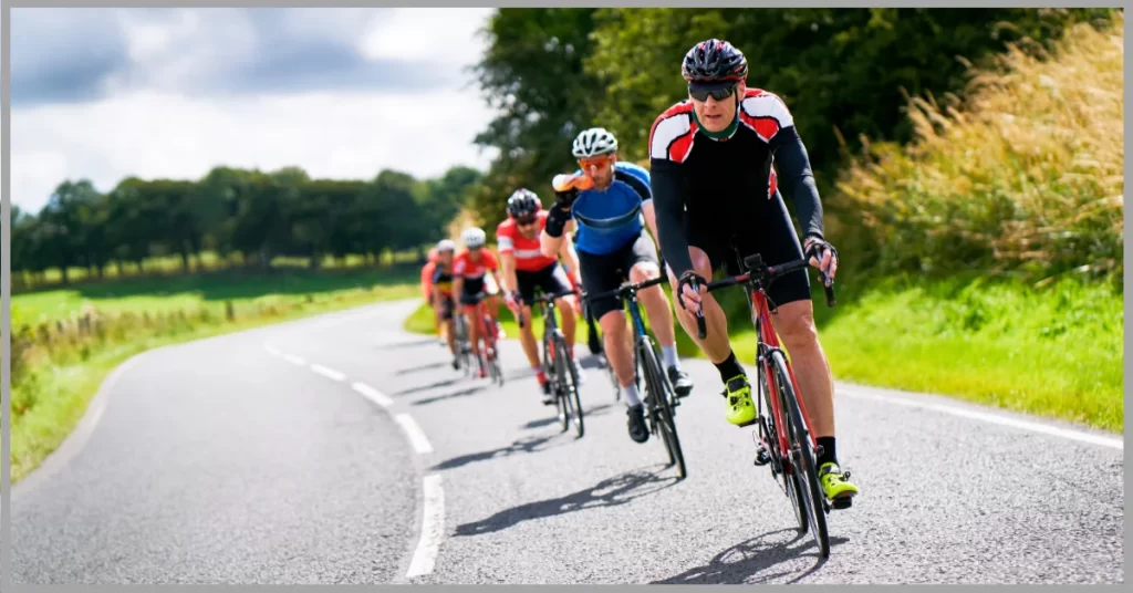 A photo realistic image of a group of cyclists on a road in a rural area, wearing colorful jerseys and helmets.