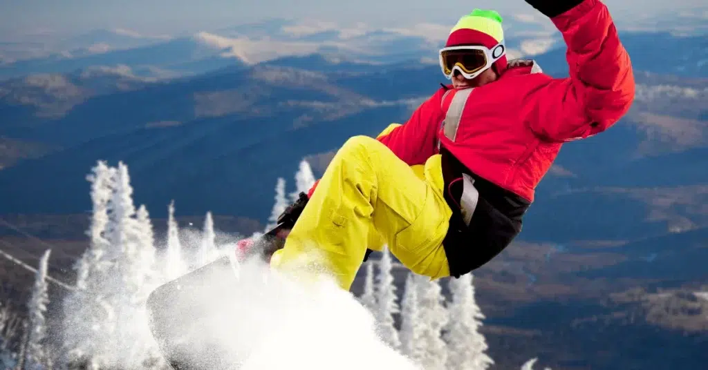 A snowboarder in bright clothing mid-jump against a scenic mountain backdrop. wearing a Technical Clothing during playing.