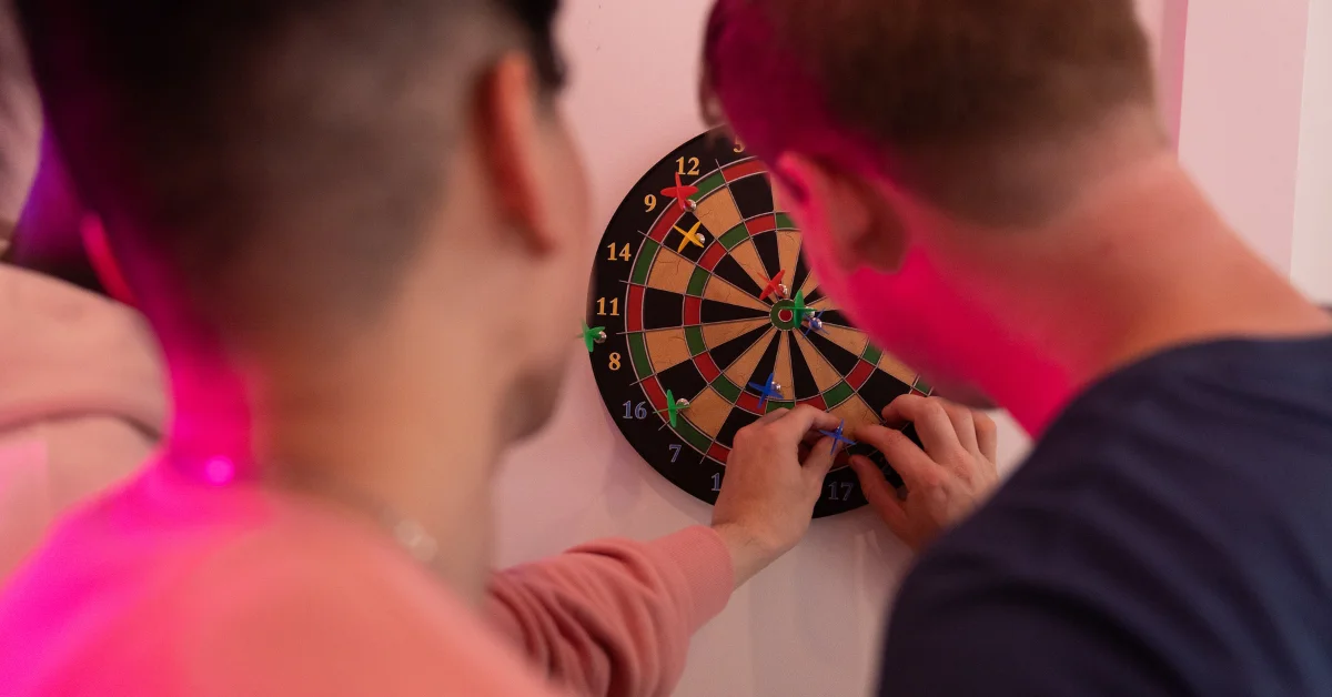 Two friends playing dart board with the right accessories.